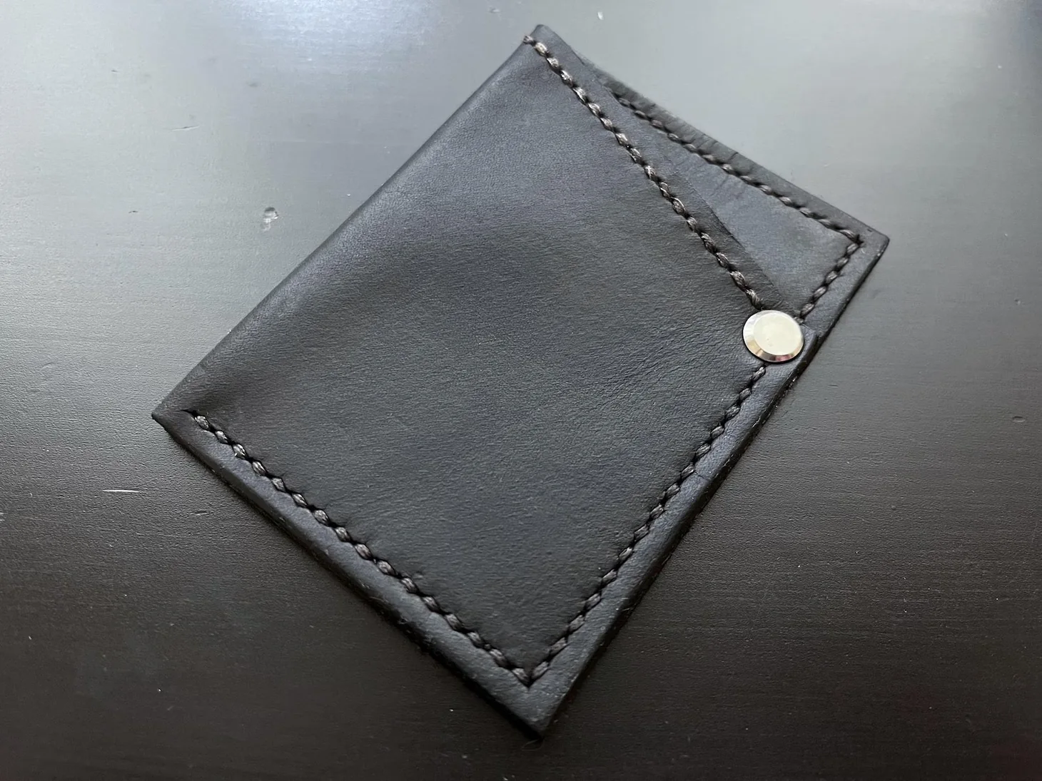 Top-down product photograph of a handmade black minimalist leather card wallet with saddle stitching.