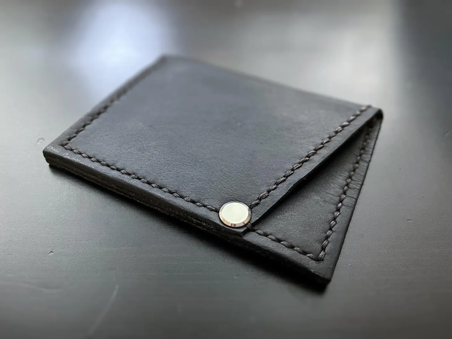 Three-quarter photograph of a handmade black leather minimalist wallet showing its folded sides and stitching.