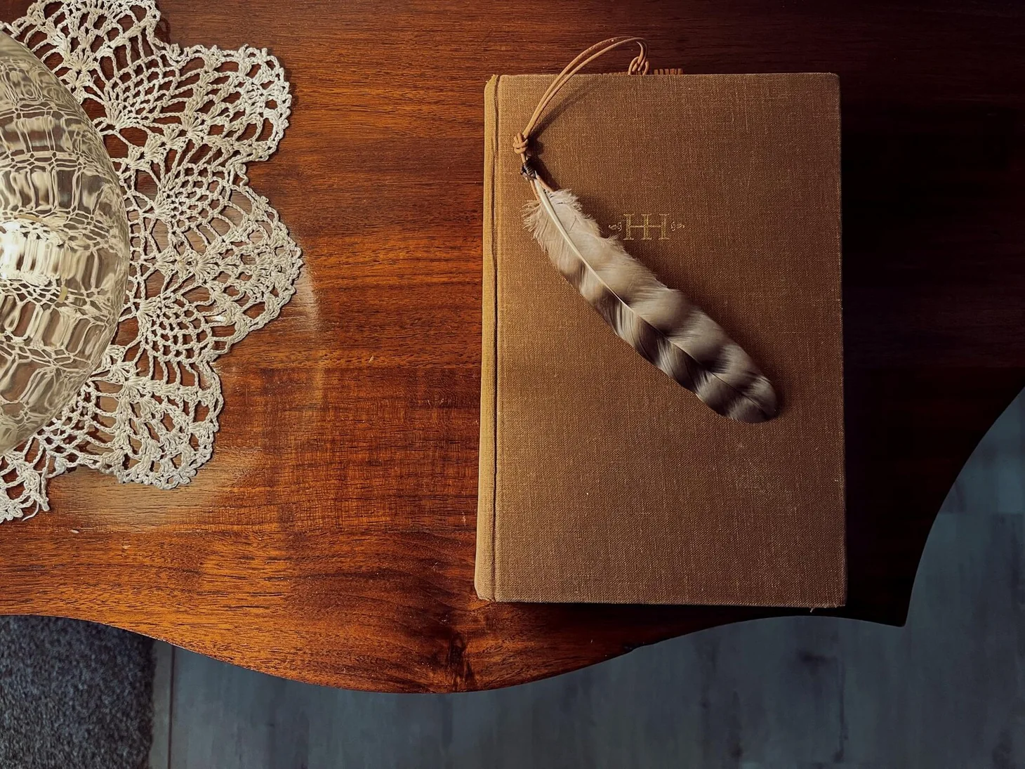 Handmade leather feather bookmark resting on an old clothbound book on a wood tabletop.
